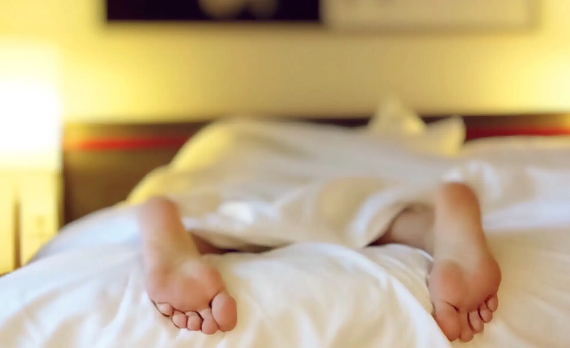 in image of someone in bed with their feet hanging out of the covers, showing a poor well-being in healthcare
